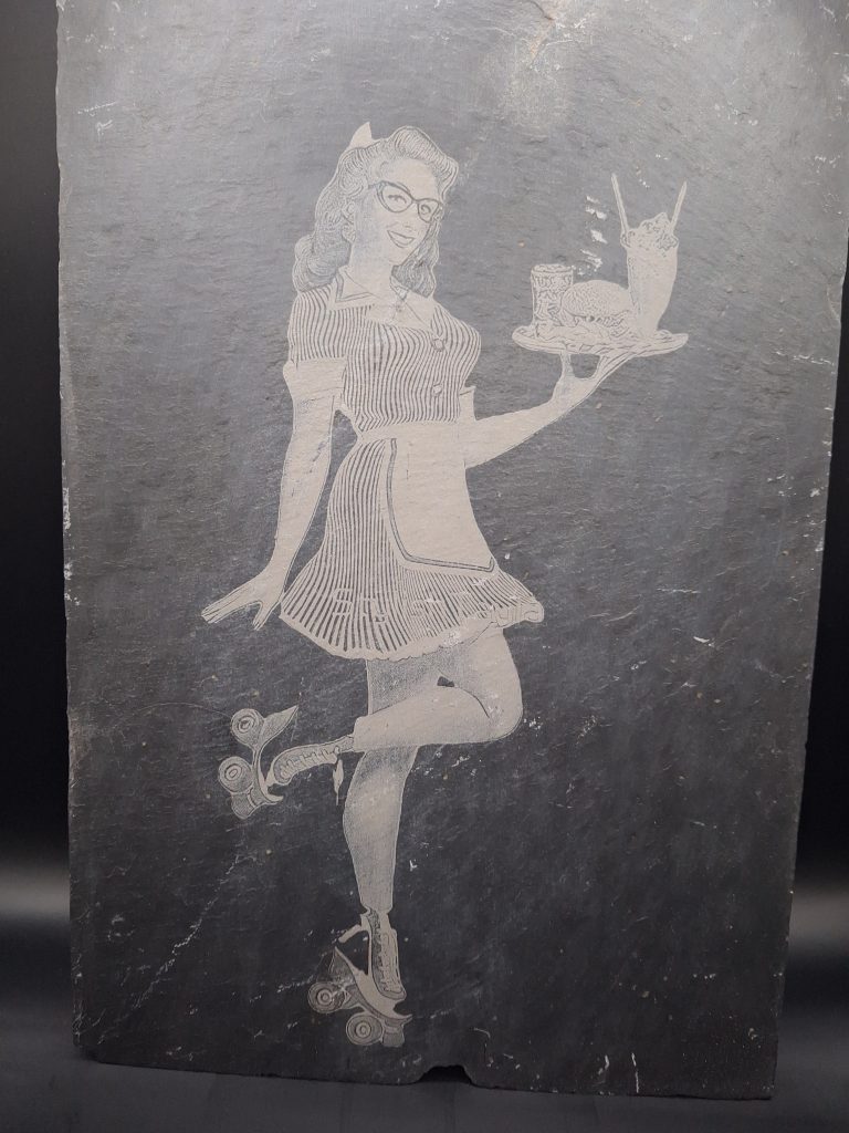 Gravure sur ardoise d'une pinup en patin à roulette tenant un plateau repas